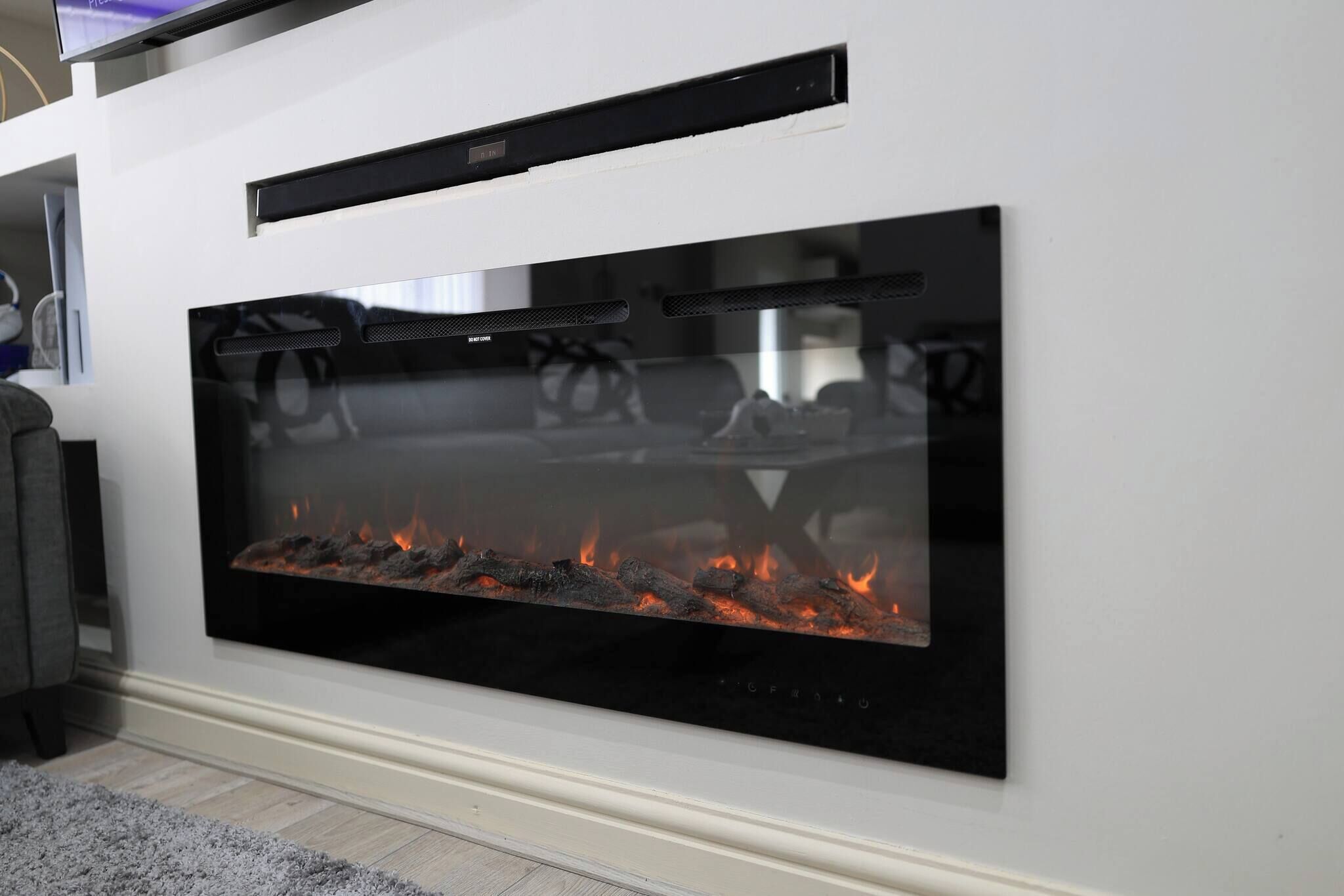 A modern fireplace with a glass front, a control panel above it, and a white wall.