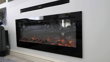 A modern fireplace with a glass front, a control panel above it, and a white wall.