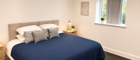 A bedroom with a bed, nightstands, a window with curtains, and a wall art piece.