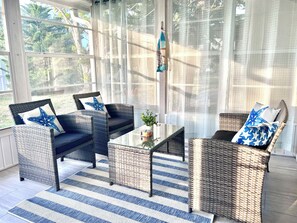 A sunlit room with wicker furniture, a striped rug, and a view through large windows. - Bright Family Villa with Community Pool Near Anna Maria Beaches & IMG Academy (Bradenton)