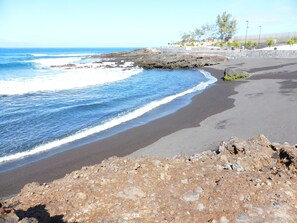 Una playa con primer plano rocoso, una orilla arenosa y una vista despejada del océano.