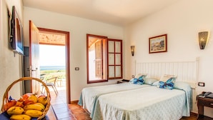 A bedroom with two beds, a wicker basket with fruit, a view through an open door, and a framed picture on the wall. - El Navio (Guia de Isora)