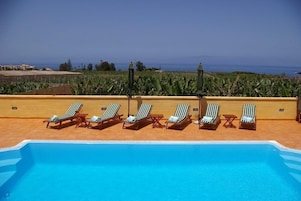 A pool with six lounge chairs and a view of the ocean.