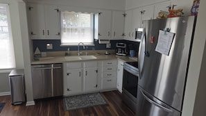 A modern kitchen with white cabinets, stainless steel appliances, and a window with blinds. - Enjoyable 2-bedroom house with boat dock across from Cranberrys. (Huntsville)