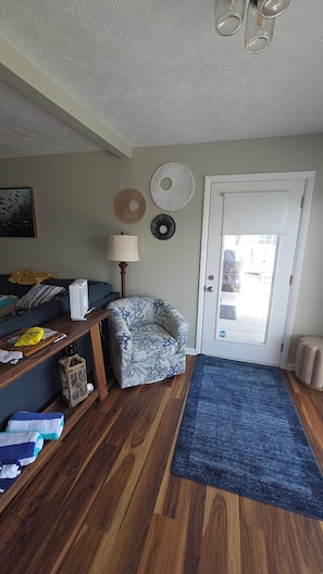 A living room with a sofa, a chair, a lamp, a door, and a blue rug. - Enjoyable 2-bedroom house with boat dock across from Cranberrys. (Huntsville)
