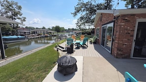 A deck with outdoor furniture, a covered grill, and a view of a canal with boats.