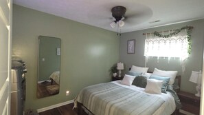 A bedroom with a bed, a ceiling fan, a mirror, a window with curtains, and a bedside table with a lamp. - Enjoyable 2-bedroom house with boat dock across from Cranberrys. (Huntsville)