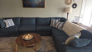 A living room with a dark blue sectional sofa, a round wooden coffee table with decorative items, and a painting on the wall.