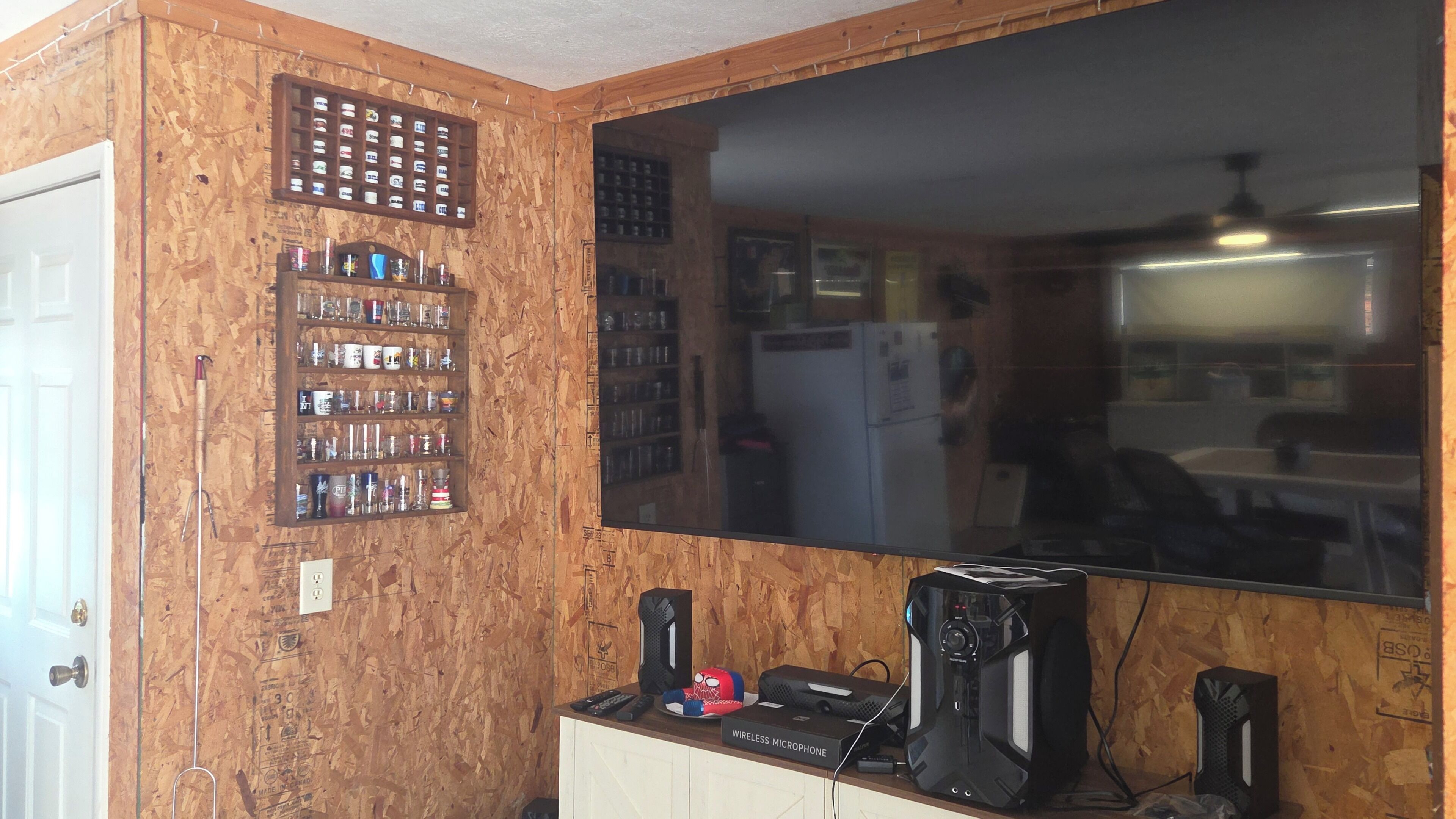 Ein Zimmer mit Holzwänden, einem großen Spiegel, einem Regal mit diversen Gegenständen und einem Schreibtisch mit elektronischer Ausrüstung.