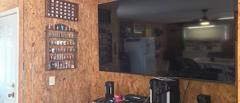 Quarto com paredes de madeira, um espelho grande, uma prateleira com diversos objetos e uma escrivaninha com equipamentos eletrônicos.