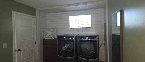 A laundry room with two front-loading washers, a wall-mounted fan, and a television.