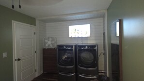 A laundry room with two front-loading washers, a wall-mounted fan, and a television.
