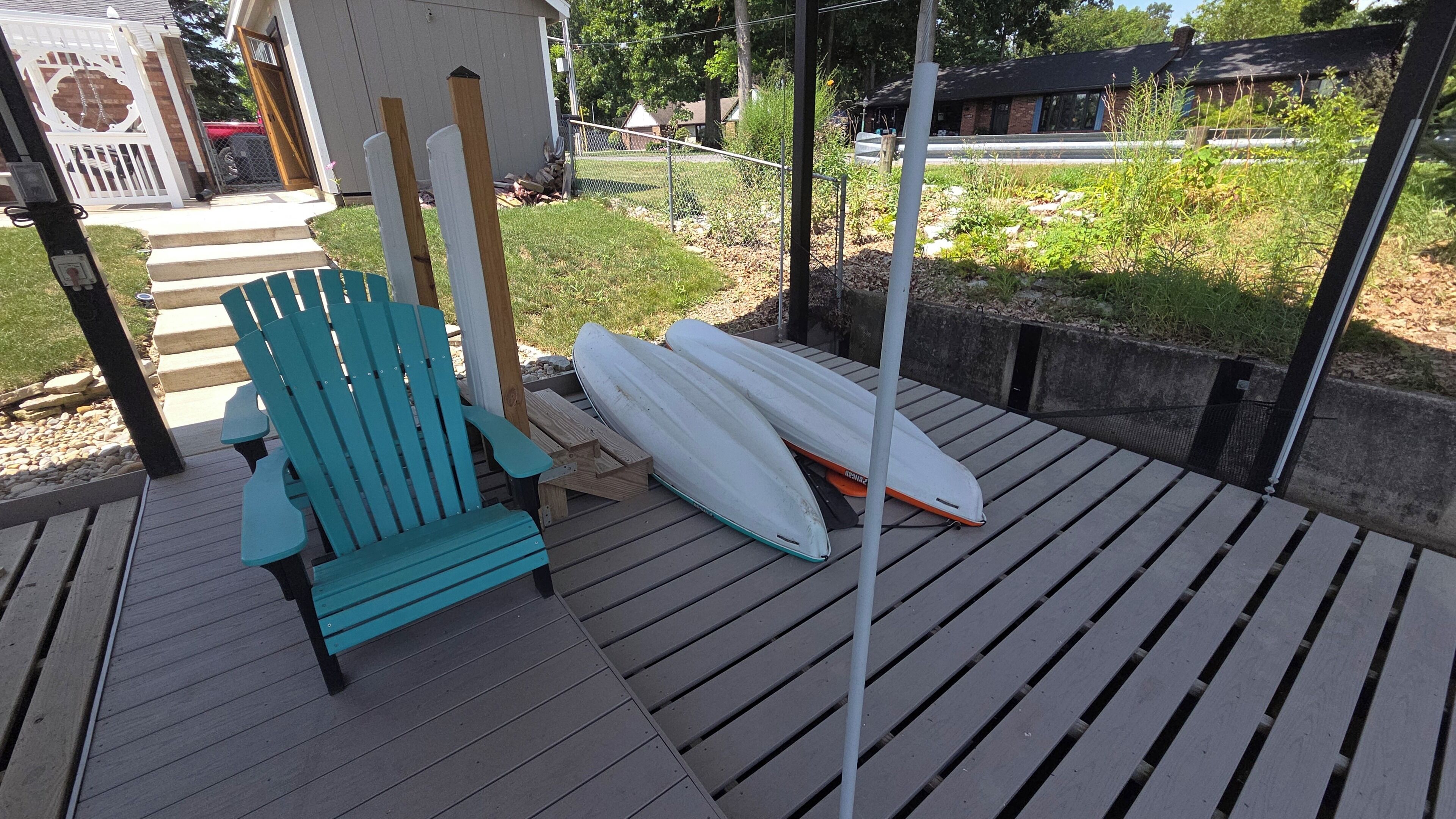 En træterrasse med en turkis Adirondack-stol og to hvide surfbrætter, der læner op ad et metalrør.