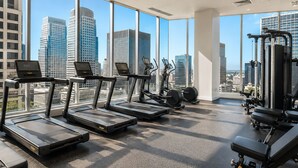 A gym with treadmills, elliptical machines, and weight equipment, large windows with a city view. - Luxury Downtown Dallas High-Rise Pool Gym & Views (Dallas)