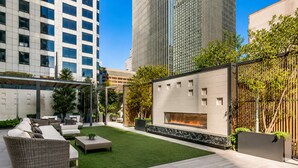 A modern outdoor patio with a fire feature, seating, and a view of tall buildings. - Luxury Downtown Dallas High-Rise Pool Gym & Views (Dallas)