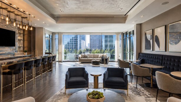 A spacious living area with a bar, seating, and large windows offering city views. - Luxury Downtown Dallas High-Rise Pool Gym & Views (Dallas)