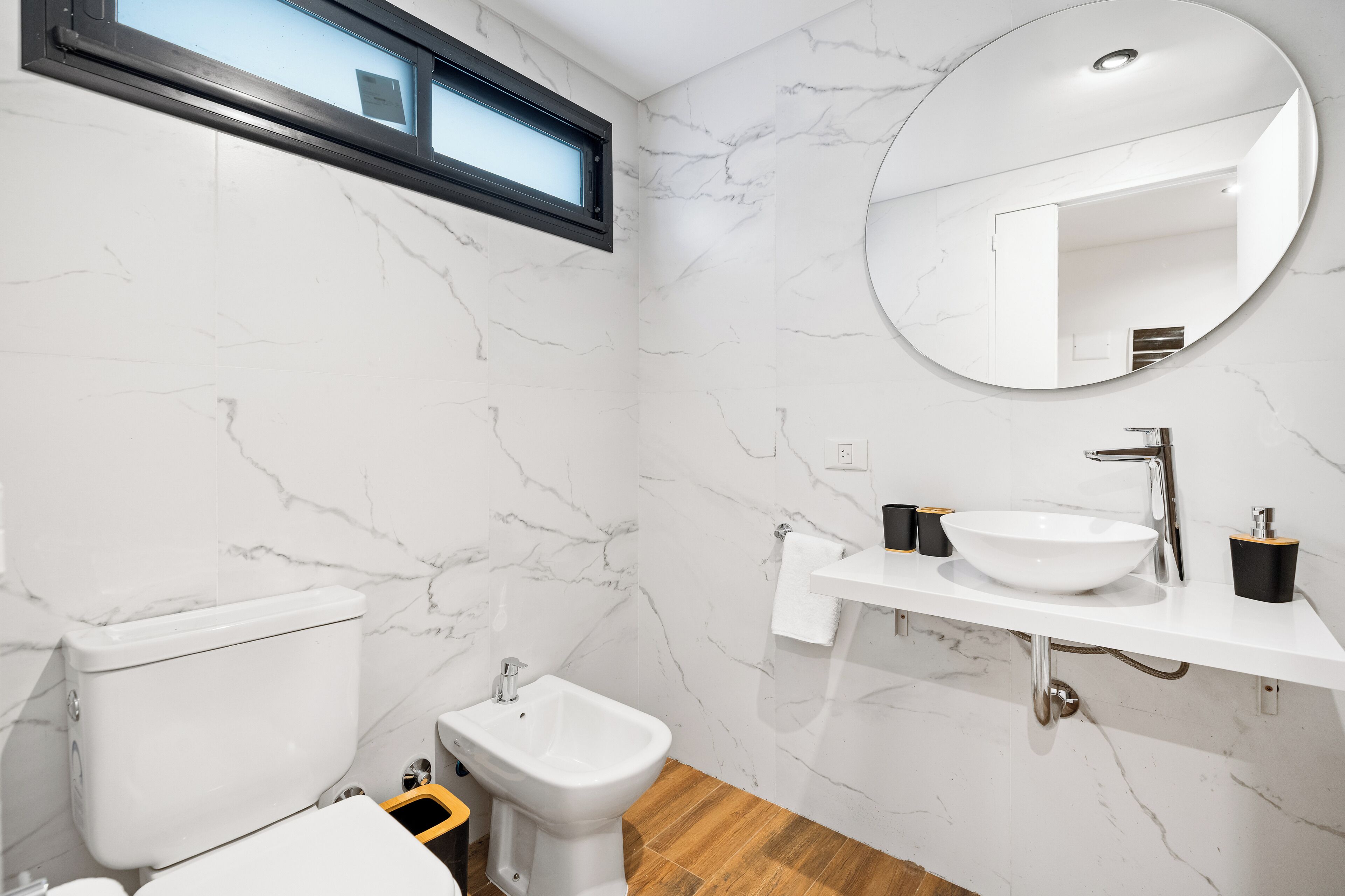 A bathroom with a toilet, bidet, sink, mirror, and marble walls.