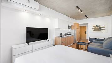 A modern hotel room with a bed, a flat-screen TV, a kitchenette, and a seating area.
