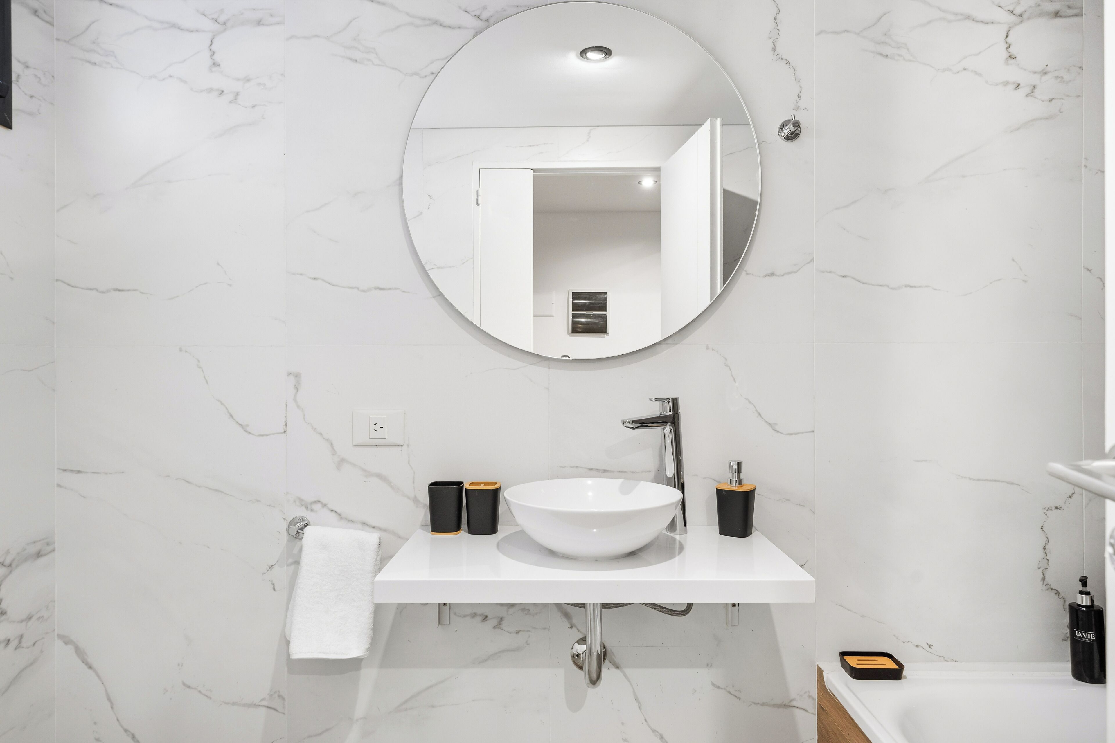 Un baño con un lavabo blanco, un espejo redondo y un perchero para toallas.