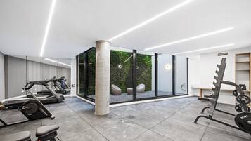 A modern gym with exercise equipment, a concrete pillar, and a glass wall with a view of greenery.