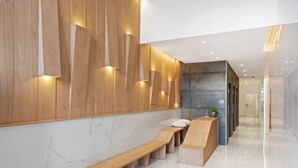 Un área de recepción moderna con un banco de madera, mostrador de recepción y una pared con listones verticales de madera e iluminación empotrada.