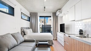 Una habitación de hotel compacta con sofá, cama, mesita, televisor y kitchenette.