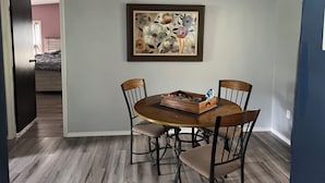 Un comedor con una mesa redonda, cuatro sillas y una obra de arte floral enmarcada en la pared.