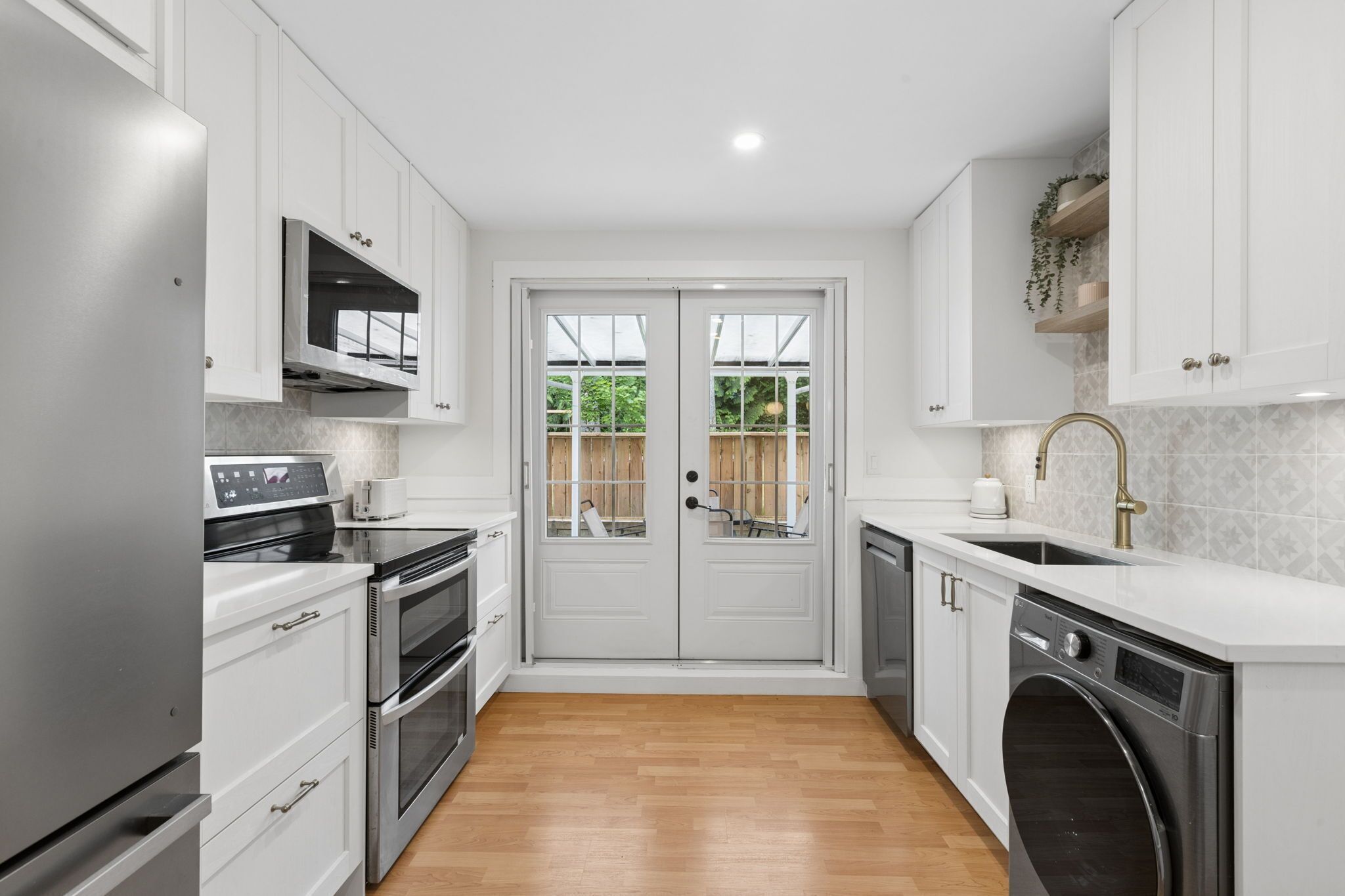 A modern kitchen with white cabinets, stainless steel appliances, a double sink, and a built-in oven.