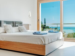 A modern bedroom with a large bed, a wooden headboard, and a view of the ocean through a large window. - Vacation home Bartok by Interhome (Jávea)