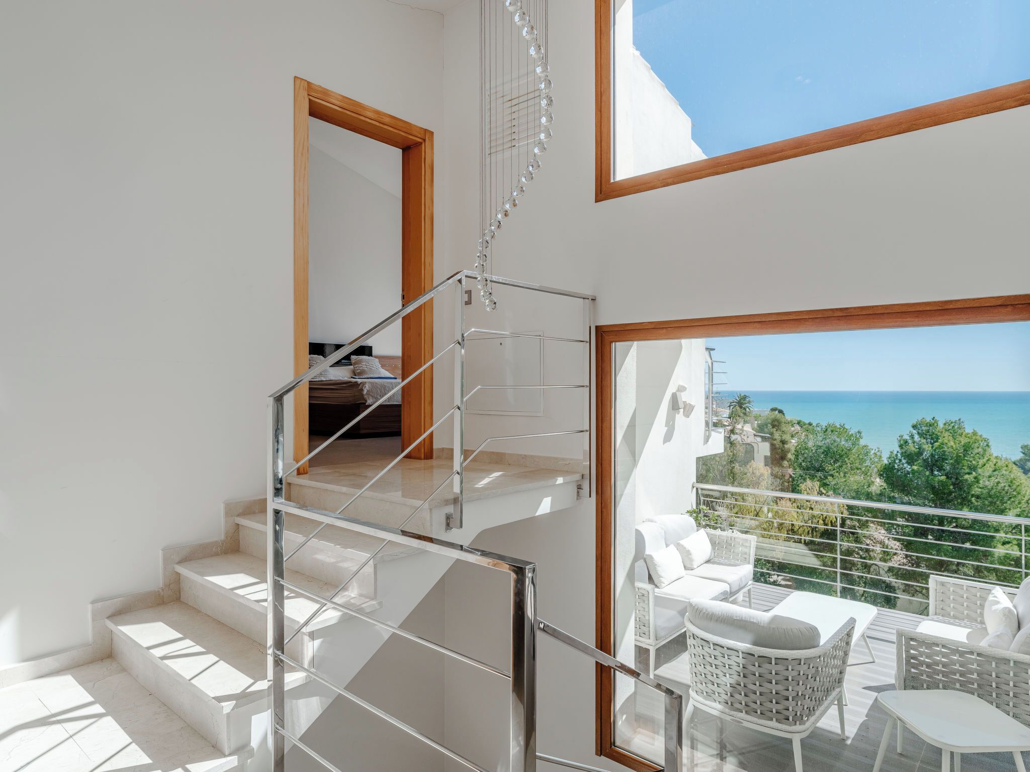 A modern interior with a staircase leading to a balcony overlooking the sea.
