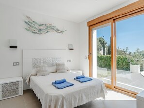 A bedroom with a bed, two bedside tables, a wall-mounted light, a decorative piece, and a sliding glass door leading to an outdoor area. - Vacation home Bartok by Interhome (Jávea)