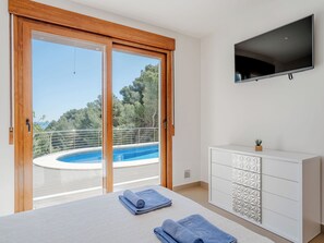 Et soveværelse med en stor skydedør til en pool, et fjernsyn monteret på væggen og et hvidt skab med skuffer.
