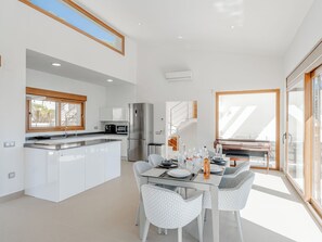 Et moderne køkken med en central ø, et spiseområde med et glasbord og mønstrede stole, og en stor skydedør til en balkon.
