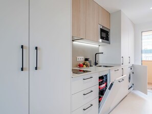 A modern kitchen with white cabinetry, a microwave, a sink, and a dishwasher. - Playa Sur by Interhome (Dénia)