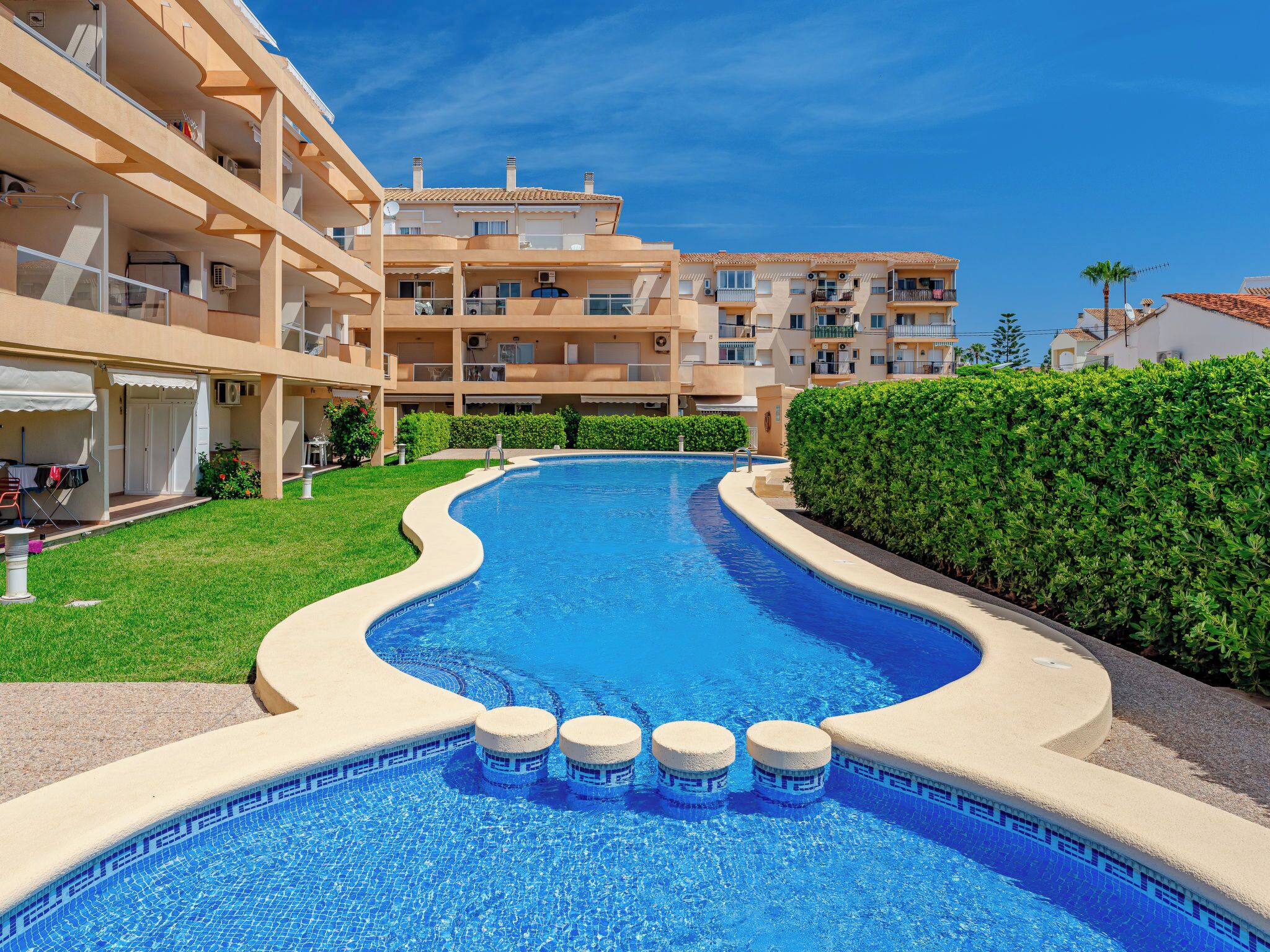 A swimming pool with a curved edge, surrounded by a well-maintained lawn and a hedge.