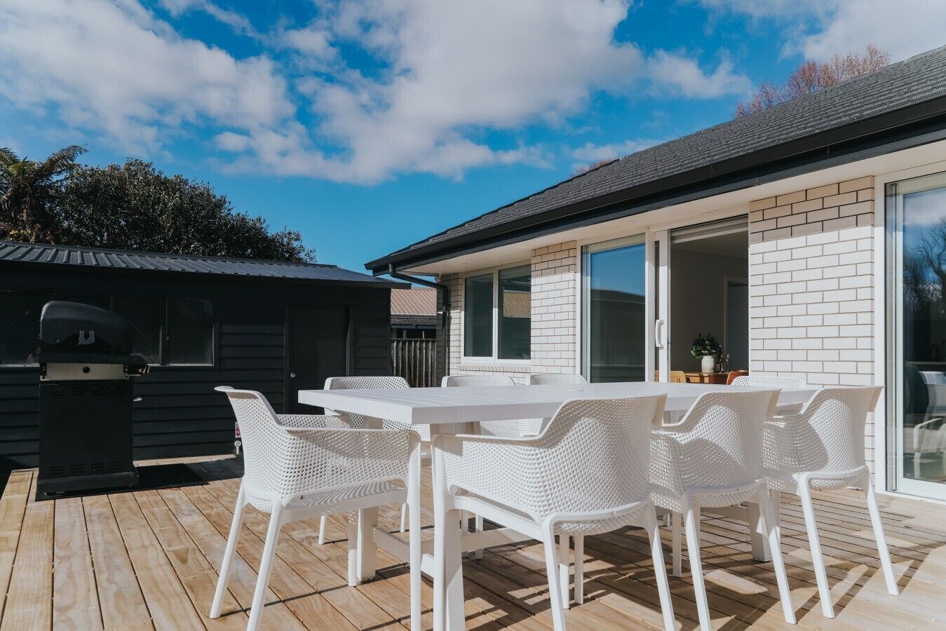 Een terras met een witte tafel en stoelen, een barbecue en een overdekt gedeelte met een zwart dak.