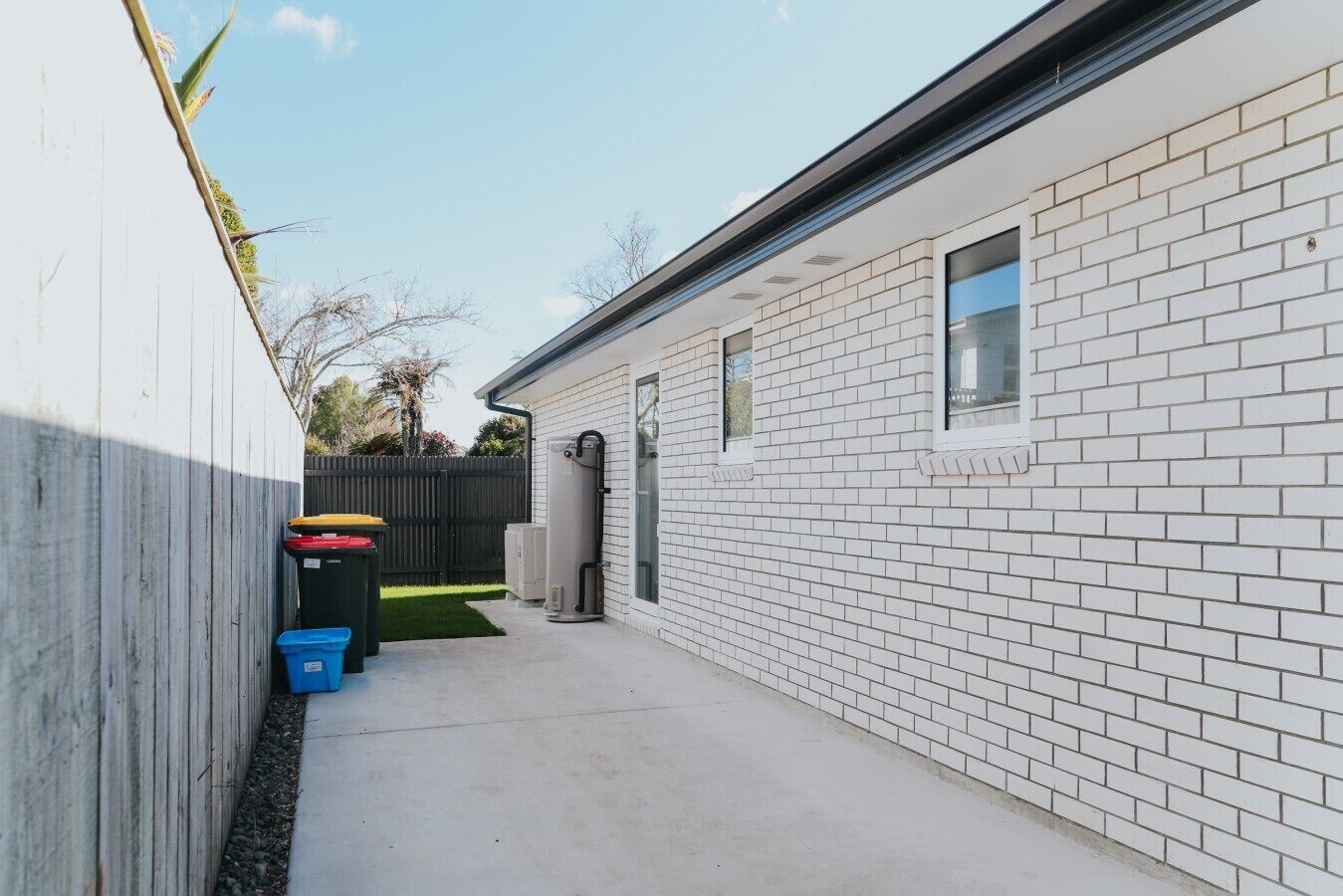 A narrow outdoor corridor with a white brick wall, a wooden fence, and a small window.