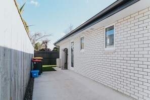 A narrow outdoor corridor with a white brick wall, a wooden fence, and a small window. - Modern Home Near the Lake | Sleeps 8, Trails on Your Doorstep (Rotorua)