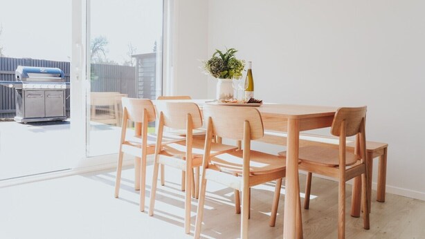 Comedor con mesa y sillas de madera, una planta en maceta y una parrilla afuera.