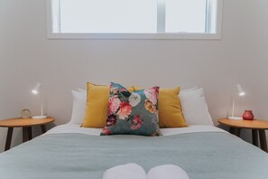 A bed with a floral pillow, two bedside tables with lamps, and a window above. - Brand new, near the lake, sleeps 8! (Rotorua)
