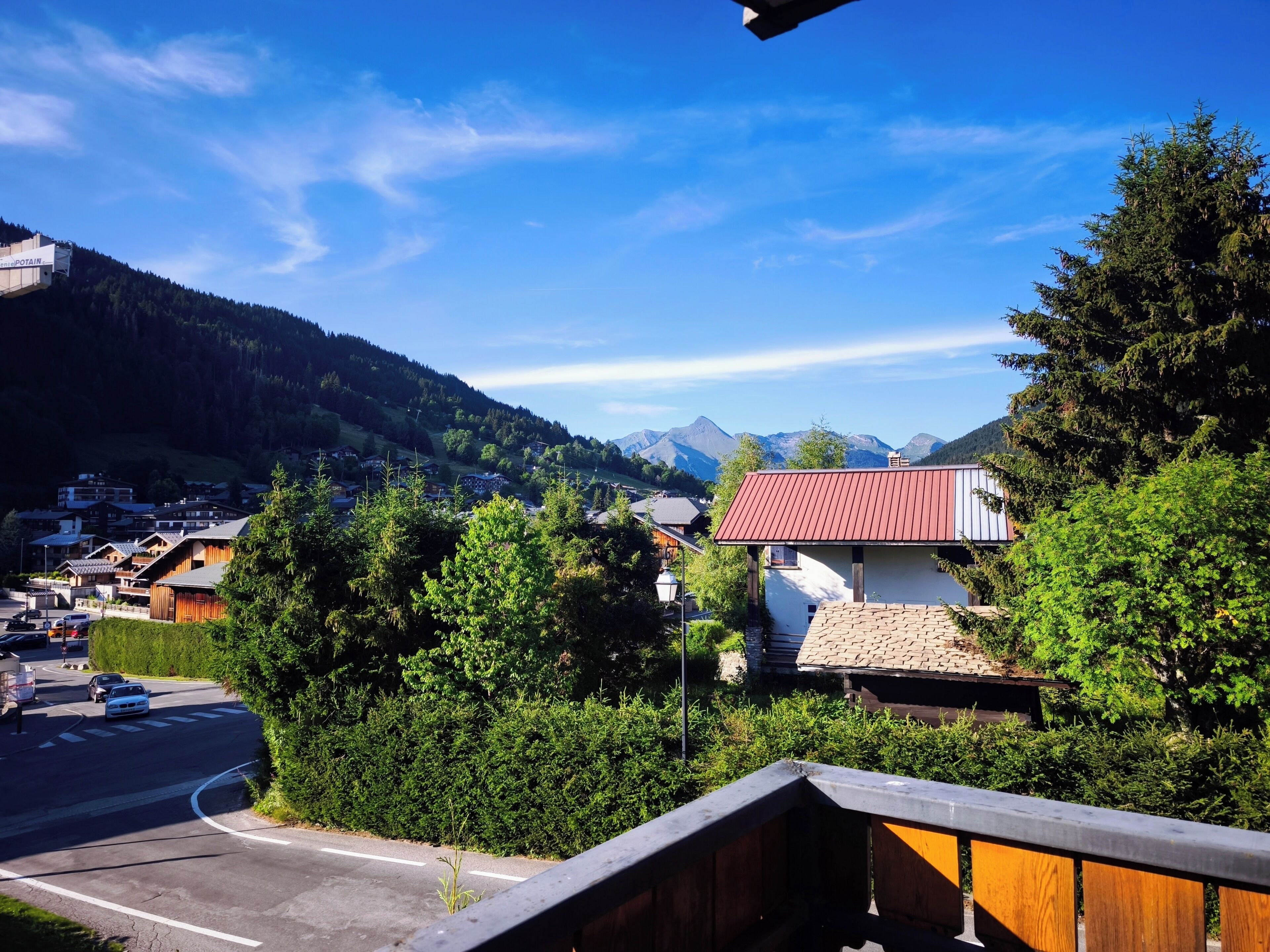 Un pueblo de montaña con casas de madera tradicionales, una carretera con coches y un cielo azul despejado.