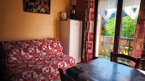 Een knus interieur met een gestreept bankje, een tafel met stoelen, een koelkast en een schilderij aan de muur.