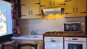 Een kleine keuken met houten kastjes, een ingebouwde magnetron, een gasfornuis en een vaatwasser.