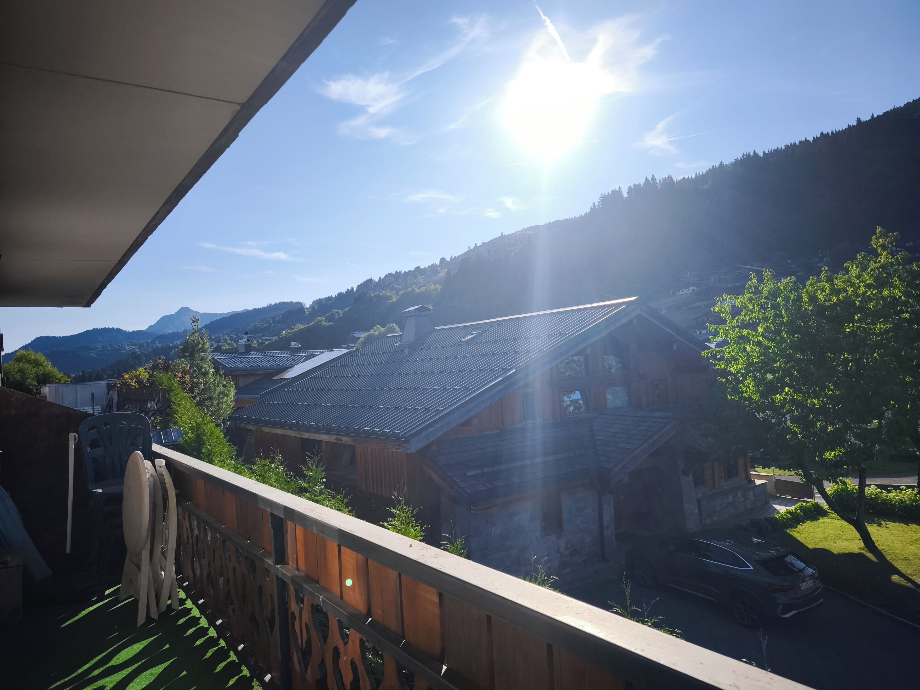 A balcony with a view of traditional wooden houses, a clear sky, and a mountain in the background.