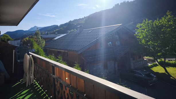 Een balkon met uitzicht op traditionele houten huizen, een heldere lucht en een berg op de achtergrond.