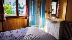 Een slaapkamer met een bed, douche, wastafel en een raam met gordijnen.