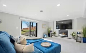 Un salon moderne avec un canapé bleu, une cheminée et un grand téléviseur fixé au mur.