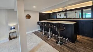 Una cucina moderna con un'area bar, pavimento in legno e un piccolo tavolino con una lampada.