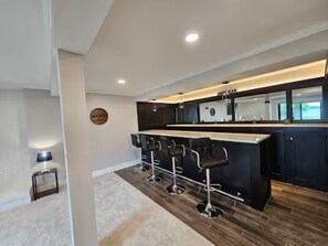 Une cuisine moderne avec un coin bar, un plancher en bois et une petite table d’appoint avec une lampe.