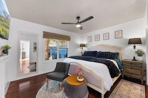 A bedroom with a bed, a chair, a side table, a lamp, a mirror, and a window with a view of the outside. - Luxury French-Inspired Retreat • Private Terrace (Kelowna)